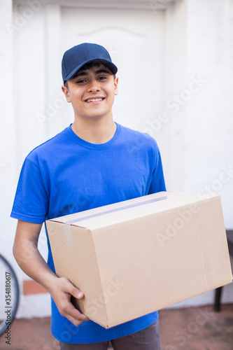 Joven repartidor amigable entrega caja de cartón en casa photo