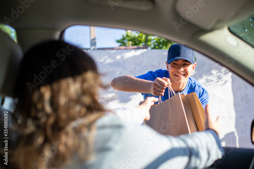 Joven trabajador de restaurante entregando comida en bolsas de cartón a la cliente en su coche