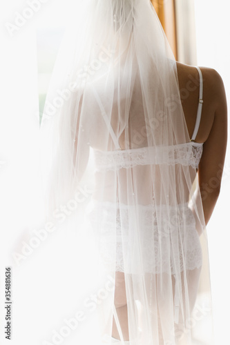 Bride with a veil on her head in lingerie. standing by the window. © gladiusstock