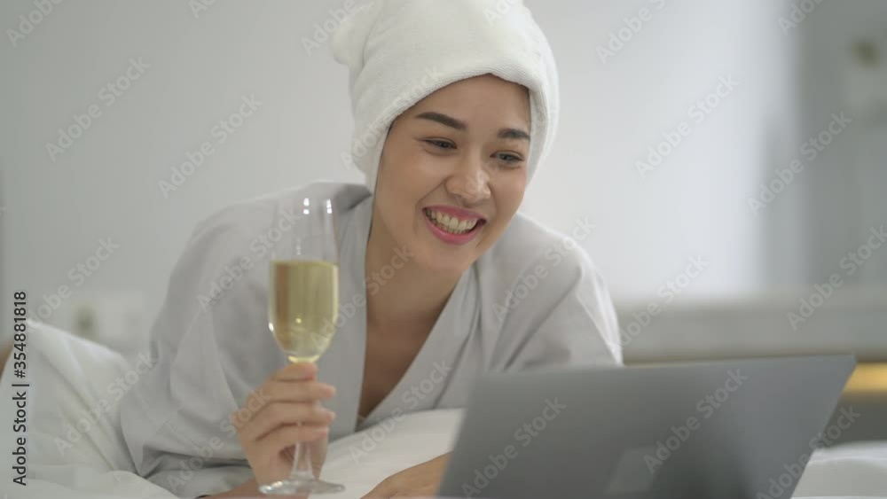 attractive girl with bath towel on head Drinks Alcoholic beverage and using laptop talking her friend in white bed attractive girl with bath towel on head Drinks Alcoholic beverage and using laptop talking her friend in white bed