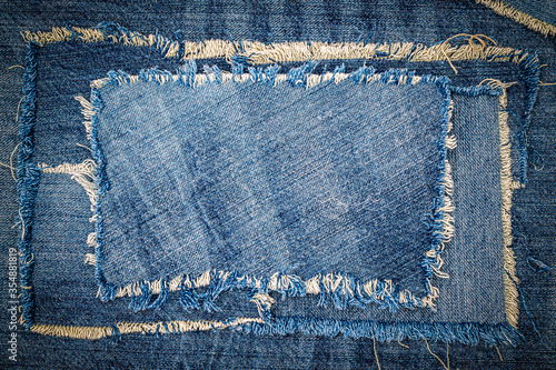 Destroyed torn denim blue jeans fabric frame on blue jeans background. Worn Jeans Casual Double Color patch Denim.