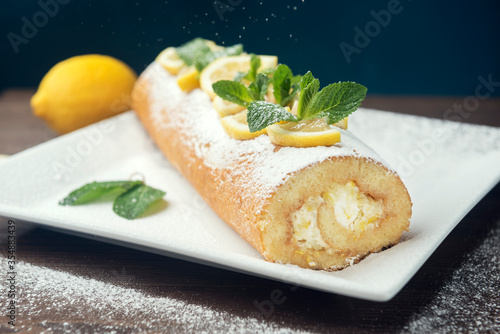Lemon roll cake decorated with slices of lemon fruit and leaves of min