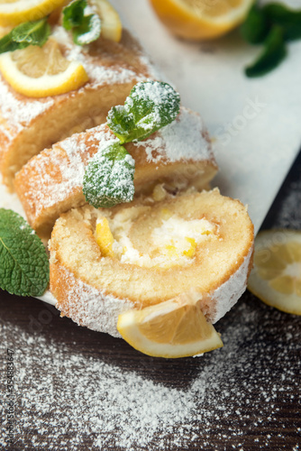 Lemon roll cake decorated with slices of lemon fruit and leaves of mint