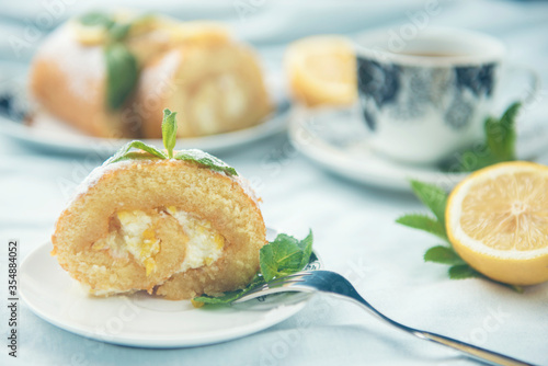 A piece of lemon roll cake decorated with slices of lemon fruit and leaves of mint © Grigoriy