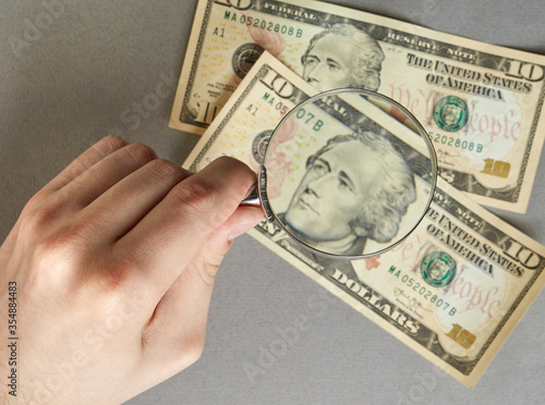 finance. hand with a magnifying glass over paper banknotes on a gray background