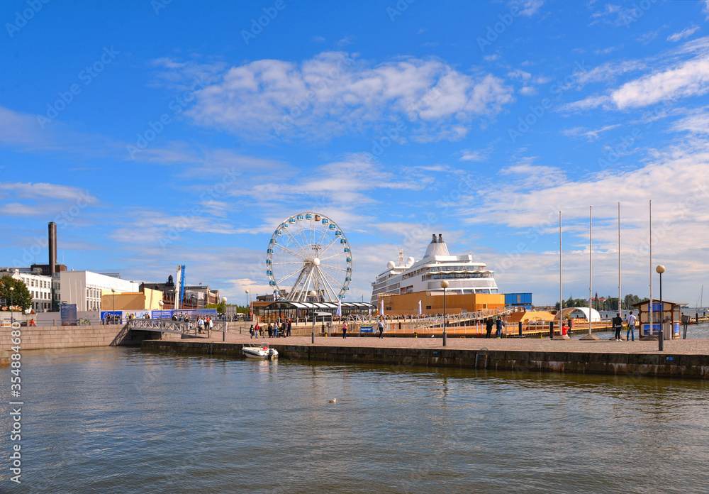 Panorama Of Embankment In Helsinki port At Summer sunny afternoon with panoramic wheel and cloudy blue sky in background, Finland