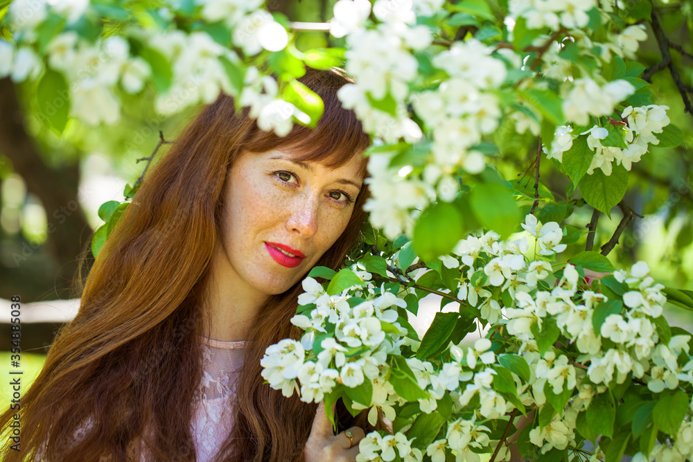 Young red-haired woman posing against the backdrop of a blossoming apple tree Young red-haired woman posing against the backdrop of a blossoming apple tree