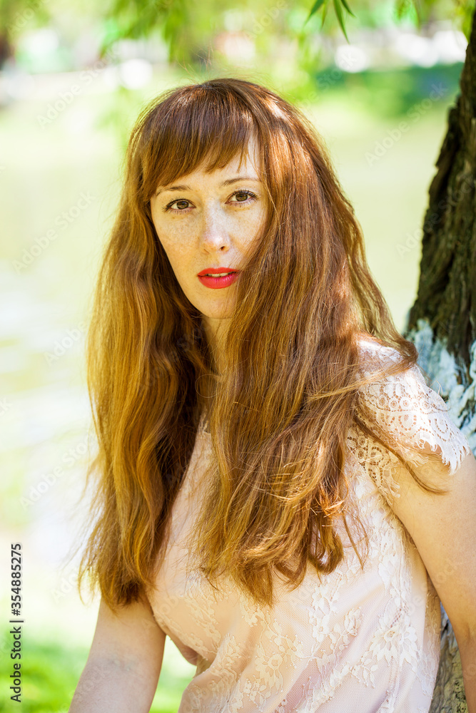 Naklejka premium Portrait of a young beautiful redhair girl on the background of tree bark
