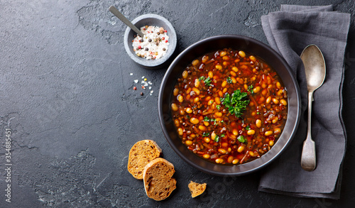 Bean soup in a black bowl. Grey background. Copy space. Top view.