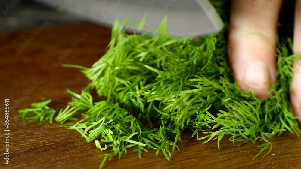Chef finely chop fresh juicy dill with kitchen knife on wooden cutting board. Close-up. Chef finely chop fresh juicy dill with kitchen knife on wooden cutting board. Close-up.