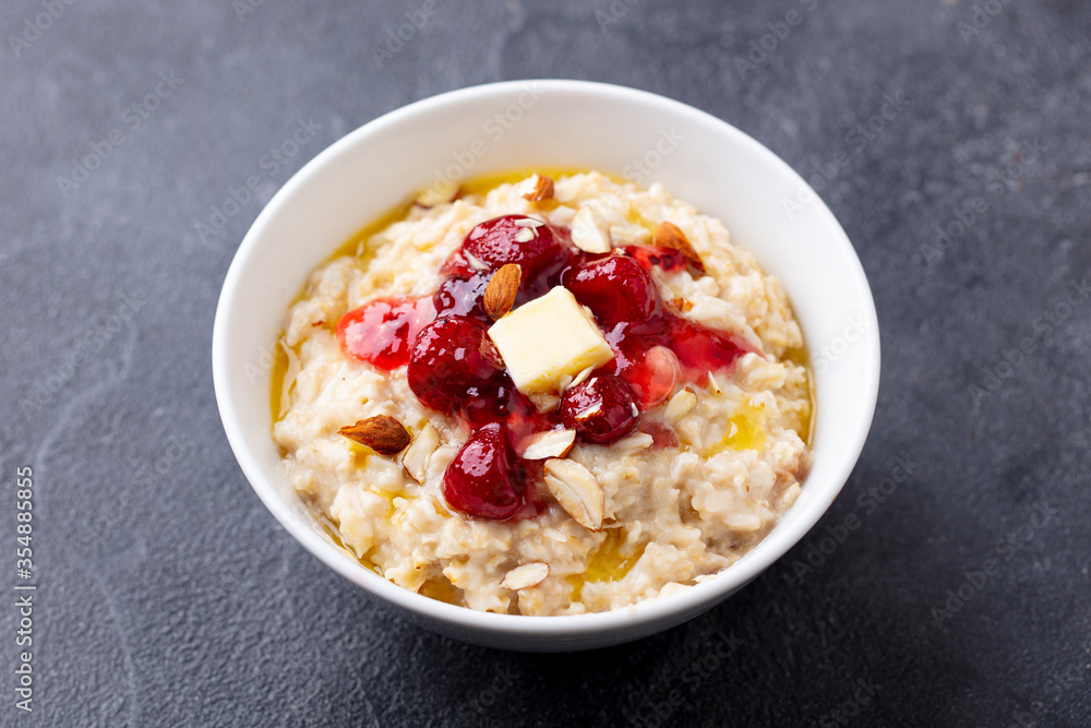 Oatmeal porridge with butter and strawberry jam in white bowl. Grey background. Close up. Oatmeal porridge with butter and strawberry jam in white bowl. Grey background. Close up.