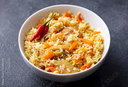 Chicken and rice pilaf, plov on white bowl. Grey background. Close up.