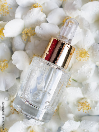 bottle with cosmetic serum on a background of jasmine flowers. Jasmine essential oil