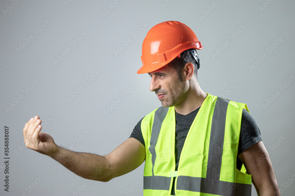 operaio con caschetto protettivo arancione e gillet giallo da delle indicazioni con le mani, isolato su sfondo grigio
