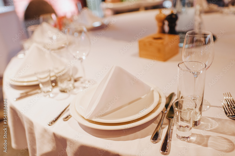 Restaurant, banquet, table setting. The table is covered with a white tablecloth, dishes, white clean plates, cutlery, napkins, wine glasses, candles. Close-up. Restaurant, banquet, table setting. The table is covered with a white tablecloth, dishes, white clean plates, cutlery, napkins, wine glasses, candles. Close-up.
