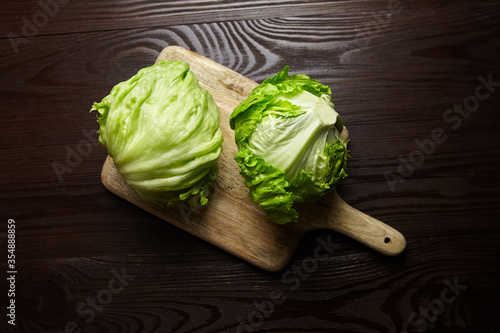 Iceberg lettuce on cutting board on wooden table background. Whole heads of fresh crisphead lettuce photo