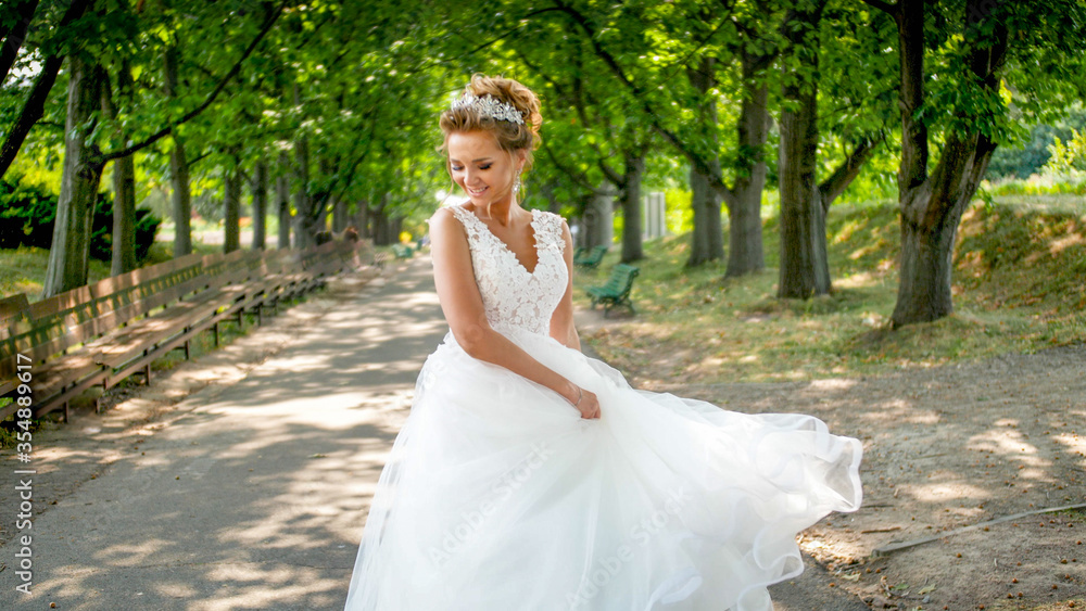 Portrait of happy smiling young bride walking in park and waving with long white bridal dress Portrait of happy smiling young bride walking in park and waving with long white bridal dress