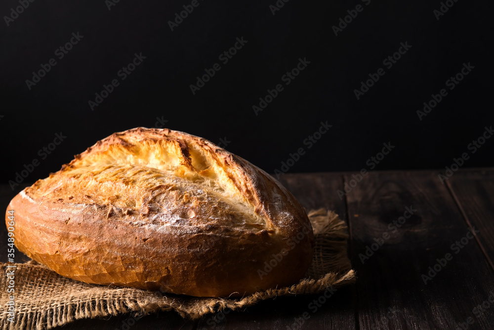 Bakery - gold rustic crusty loaves of bread and buns on black background.