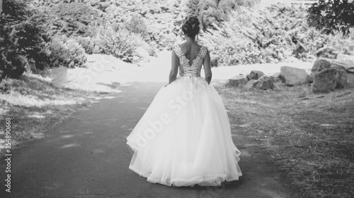 Black and white photo of elegant young bride in long dress walking at park