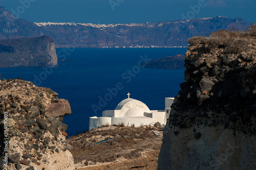 typical white church in santorini. in the background you can see the villages at the top of the cliffs of the island