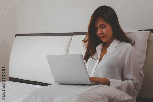 Relaxing work at home, concept with a women sitting on the bed with laptop and other tools.