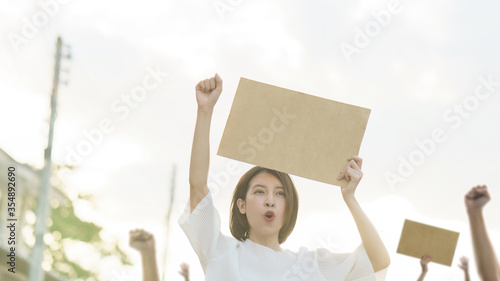 Woman holding a blank placard to put the text at protesting. People with her hands raised in the air.
