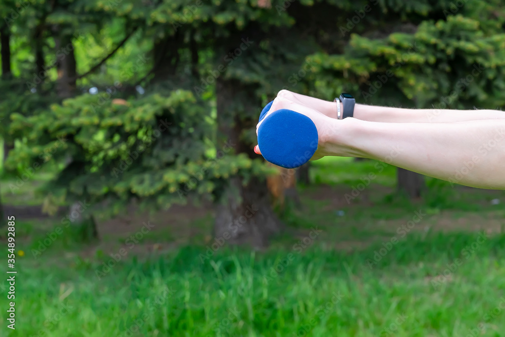 Elongated female hands with dumbbells on a background of trees Elongated female hands with dumbbells on a background of trees