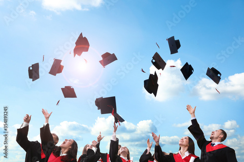 Happy students throwing graduation hats in air outdoors
