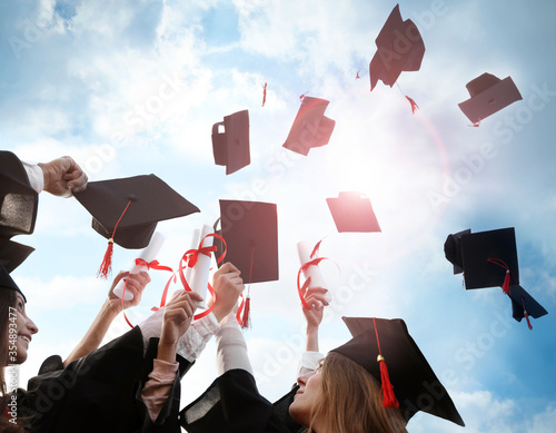 Cuadro en lienzo Happy students with diplomas throwing graduation hats in air outdoors