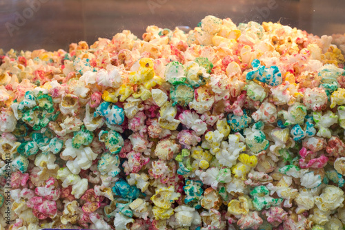 Close-up texture of multi-colored popcorn in a glass movie theater container. Popcorn with a variety of colors and flavors.