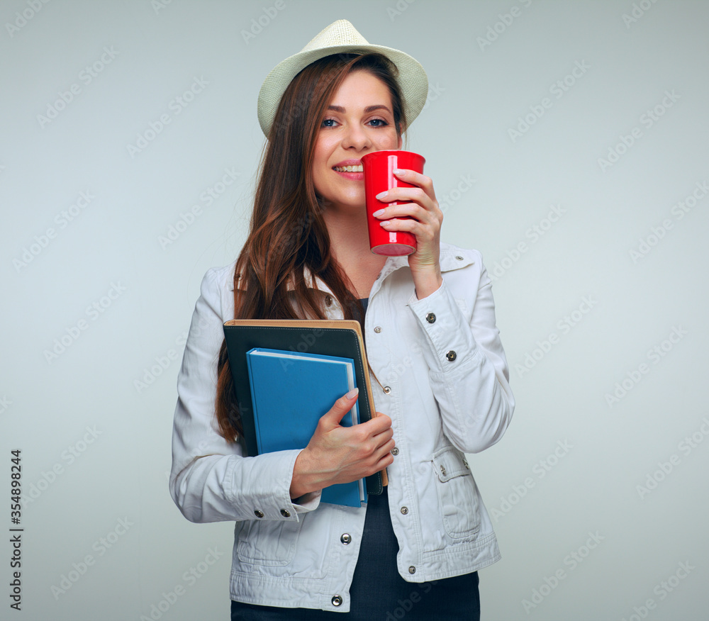 Woman student dressed white jacket and holding big red coffe cup and books.