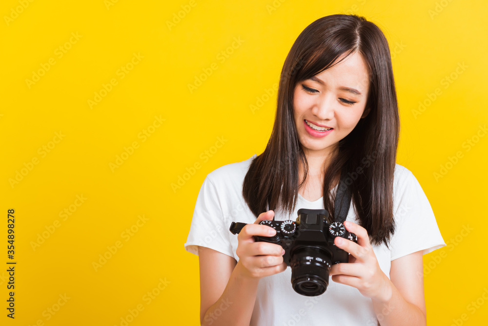 Portrait of happy Asian beautiful young woman photographer review picture she seeing a photo on the screen of digital mirrorless photo camera after photography, isolated on yellow background Portrait of happy Asian beautiful young woman photographer review picture she seeing a photo on the screen of digital mirrorless photo camera after photography, isolated on yellow background