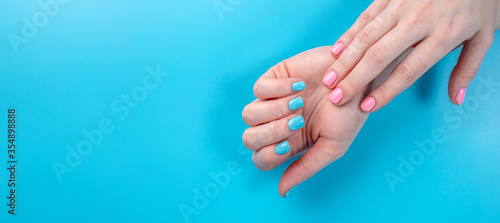 Women's hands with bright summer manicure on a blue background. Trendy colors of nail polishes for young women. Copy space