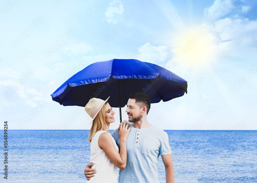 Happy romantic couple with umbrella for sun protection near sea