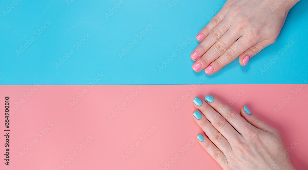Fototapeta premium Women's hands with bright summer manicure on a blue and pink background. Trendy glamorous nails in fun colors