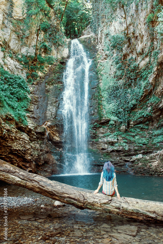 Girl with blue hair resting in front of waterfall in summer.