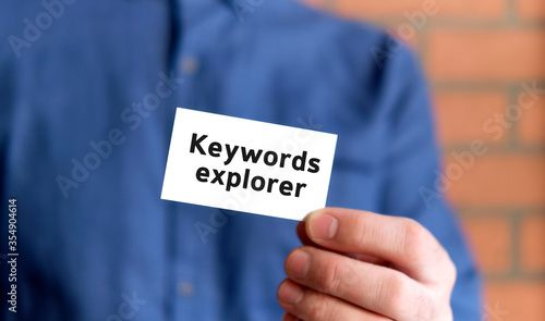 A man in a blue shirt holds a sign with the text of keywords explorer in one hand