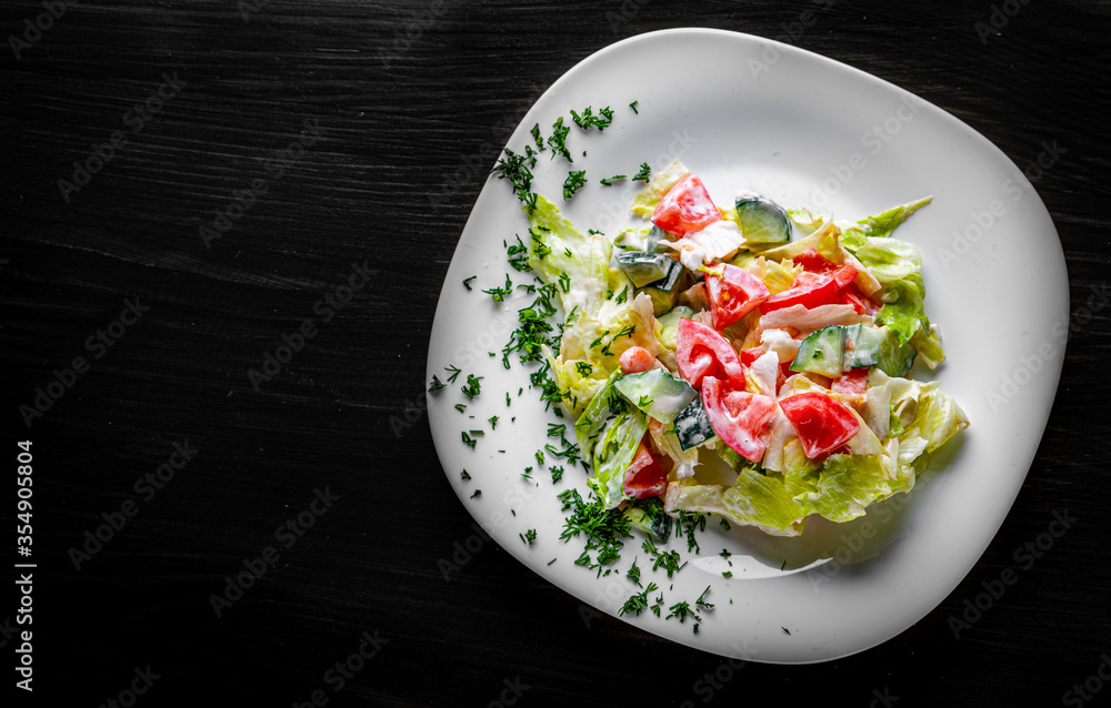 fresh vegetable salad with tomato and cucumber in white plate on black wooden table background