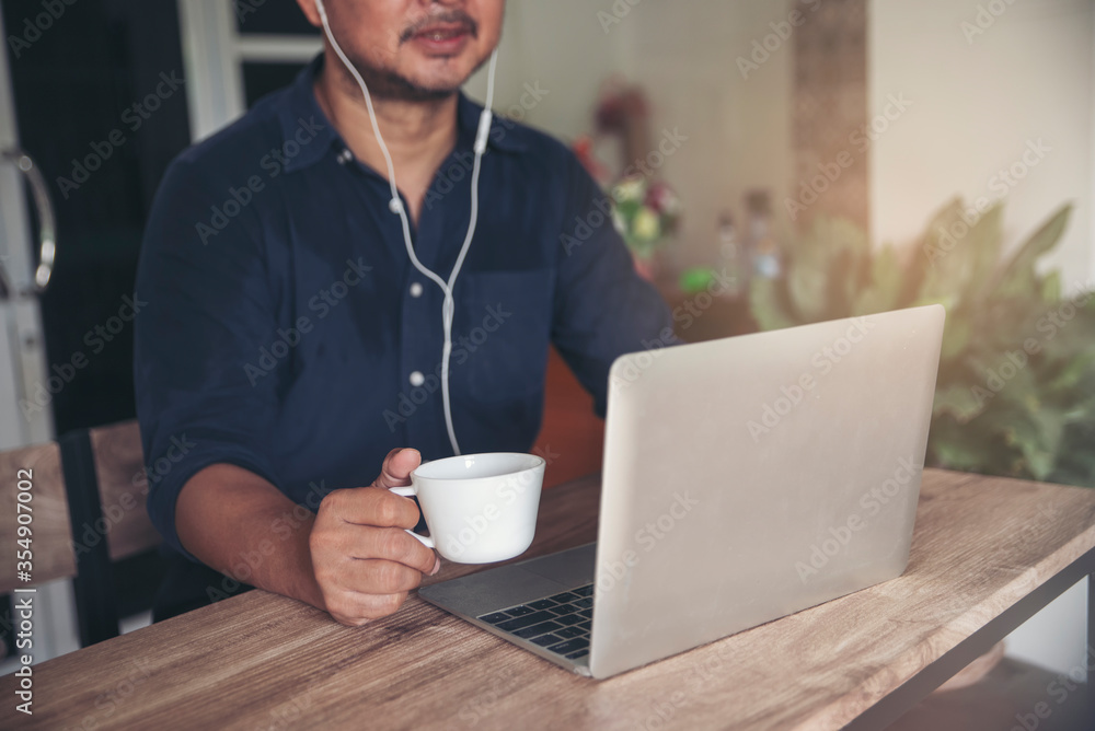 Businessman working online at the home office by laptop. Asian young entrepreneurs watching webinars and talking during meeting video conferences calls with team, and drinking coffee Businessman working online at the home office by laptop. Asian young entrepreneurs watching webinars and talking during meeting video conferences calls with team, and drinking coffee