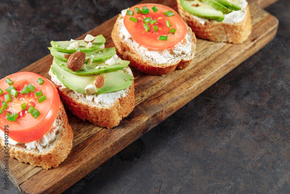 Assorted vegan bruschette snack on a wooden chopping board on a dark textured table. Mini sandwich mix. Top view, close up Assorted vegan bruschette snack on a wooden chopping board on a dark textured table. Mini sandwich mix. Top view, close up