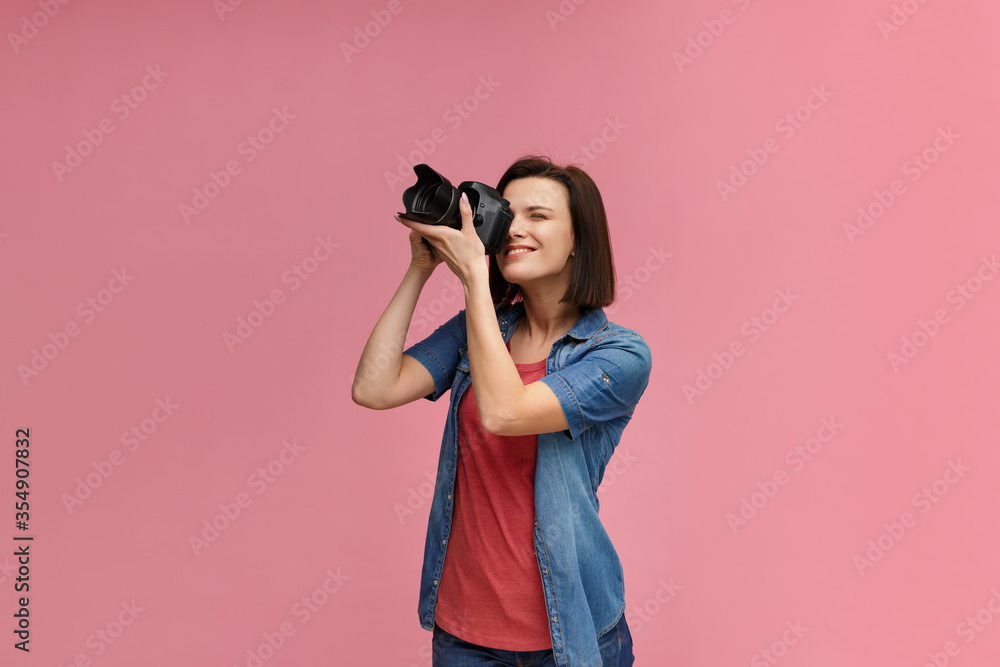 Portrait of young female photographer isolated on pink background with copy space. Photographer with professional camera taking photo in photo studio. Profession, occupation, self-employment. Portrait of young female photographer isolated on pink background with copy space. Photographer with professional camera taking photo in photo studio. Profession, occupation, self-employment.