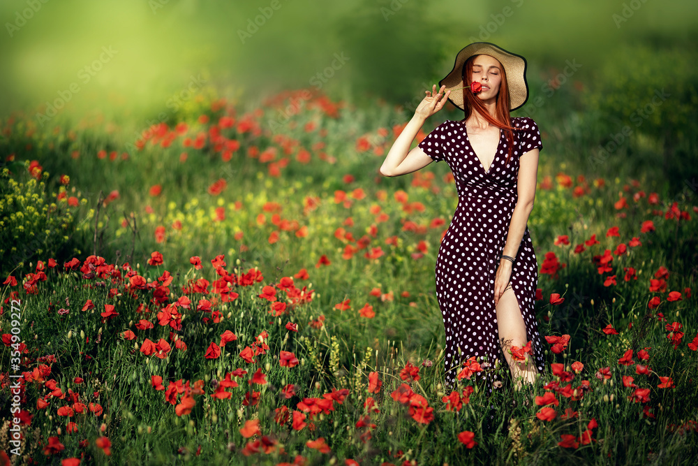 A beautiful happy woman with red hair in a straw hat and a red polka dot dress on a poppy field at sunset A beautiful happy woman with red hair in a straw hat and a red polka dot dress on a poppy field at sunset