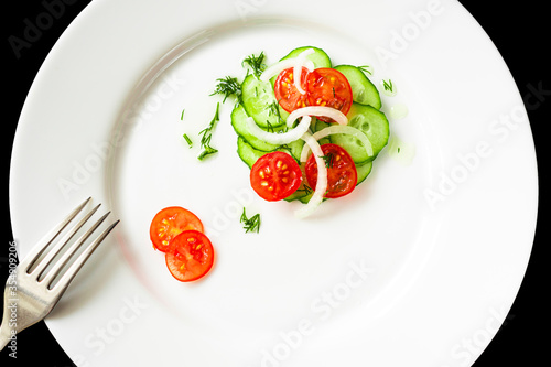 Cherry tomatoes, cucumber and onion salad on a white plate. There is a fork on the left side of the plate