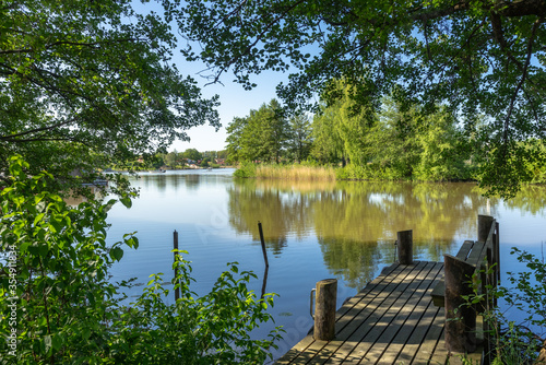 Wooden pier berth jetty with a bench for relax rest. Amazing panoramic view of the lake "Malaren" in Sweden. Calm water with beautiful reflections of green trees in summer. Foliage frame. 
