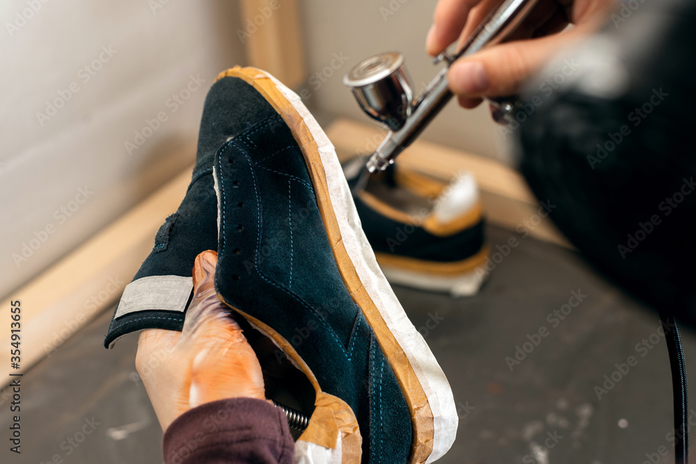 Craft man painting on a pair of shoes. Painting and restoring suede blue sneakers