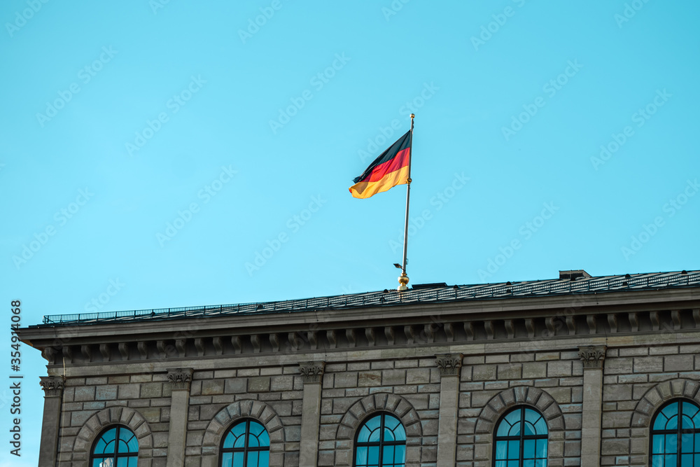 German flag waving on silver flagpole,  building in Munich.