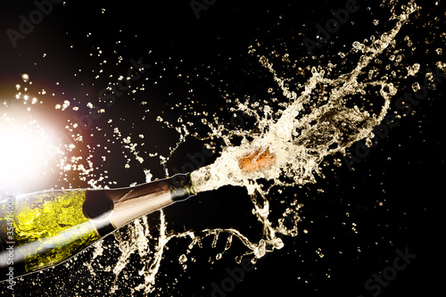 Celebration theme with splashing champagne on black background with light flare. Christmas or New Year, Valentines day background.