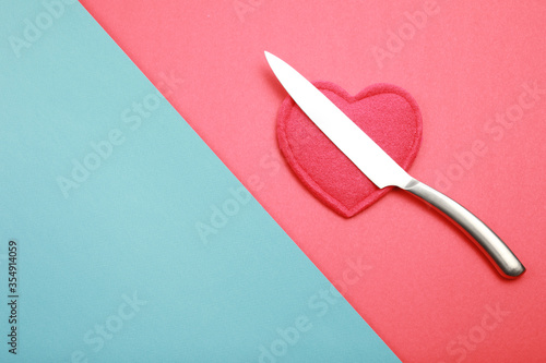 Sharpen steel knife  above red heart like symbol about dangers situation for heard isolated on red and blue background with copy space