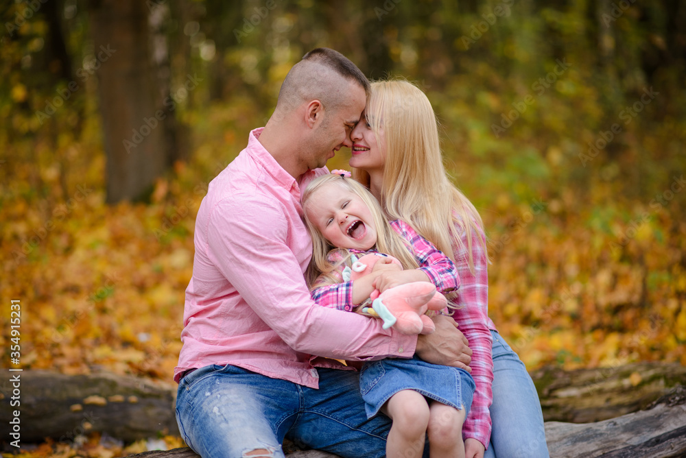 Father mother and daughter hug and sit on a log against the backdrop of an autumn park. Father mother and daughter hug and sit on a log against the backdrop of an autumn park.