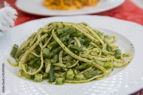 Close up view of a traditional green pasta dish: green Spaghetti with green bean and zucchini, served in a white plate